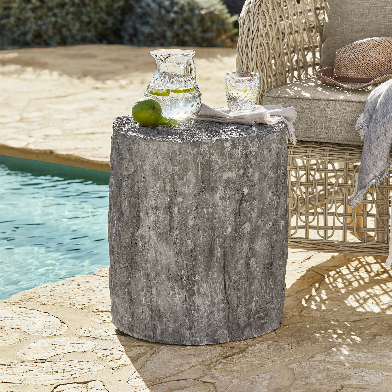 Šedý betonový stolek s texturou dřeva vedle proutěného křesla u bazénu