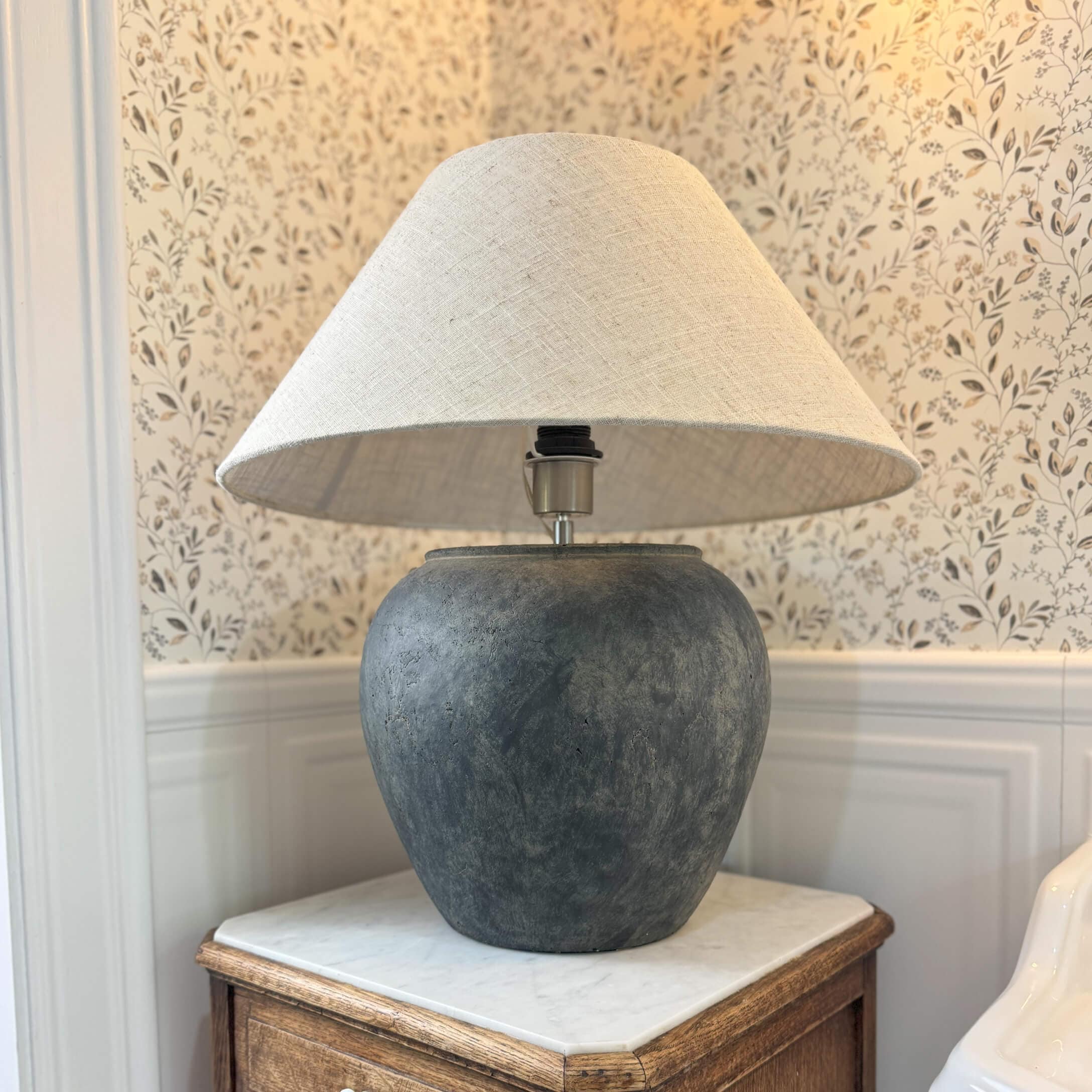 Stolní lampa z tmavě šedé keramiky s béžovým stínidlem na dřevěném stolku v klasickém interiéru