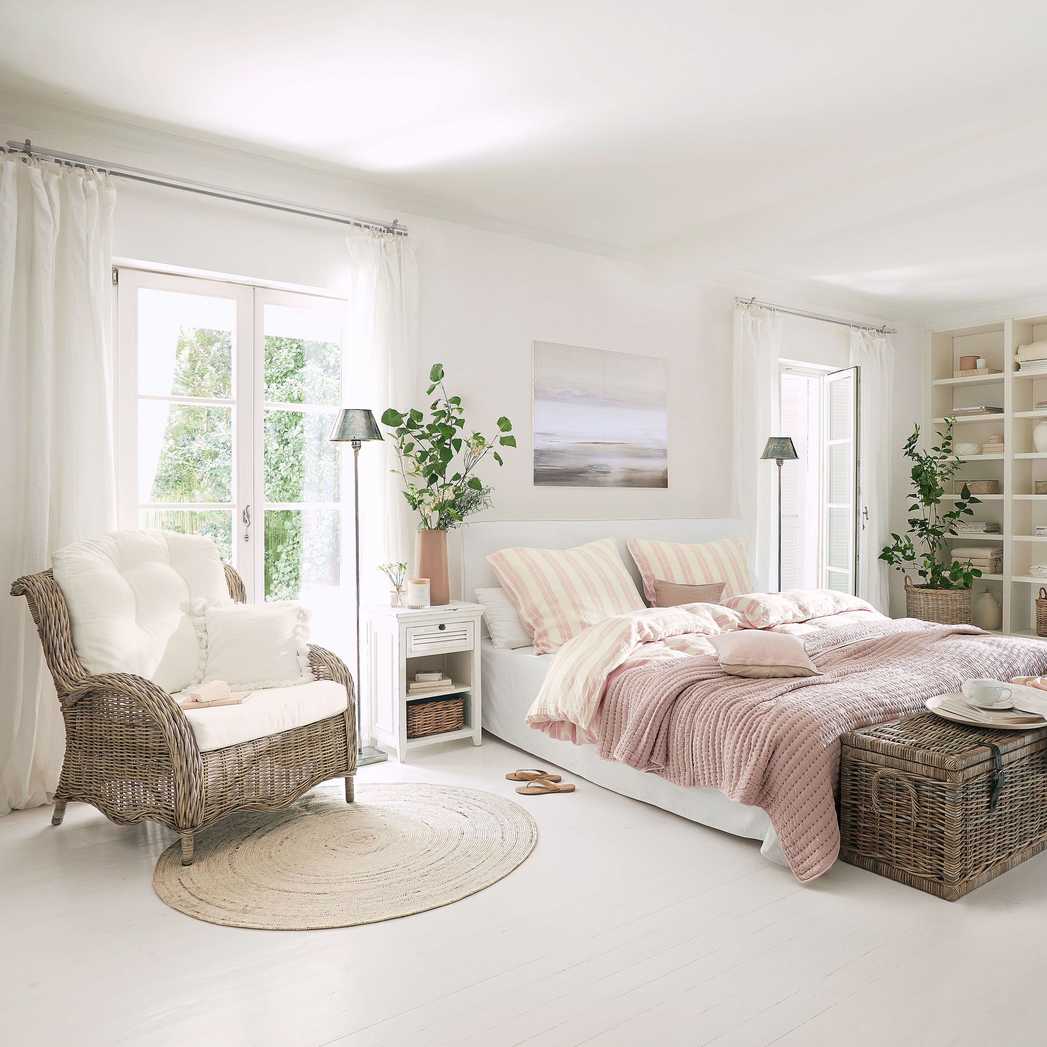 Světla ložnice s bílou postelí, růžovým povlečením a proutěným křeslem na světlé podlaze